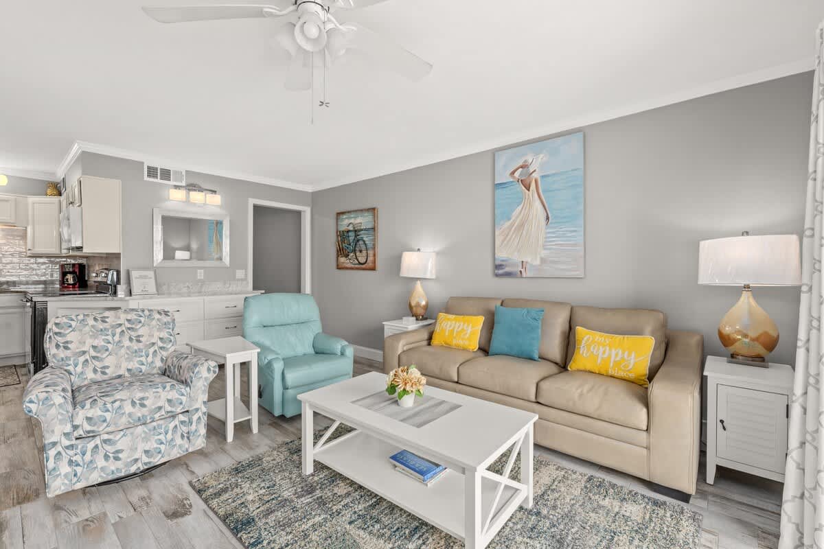 The Summit 228 – Living room with a beige sofa, patterned chair, coffee table, and kitchen area visible in the background.