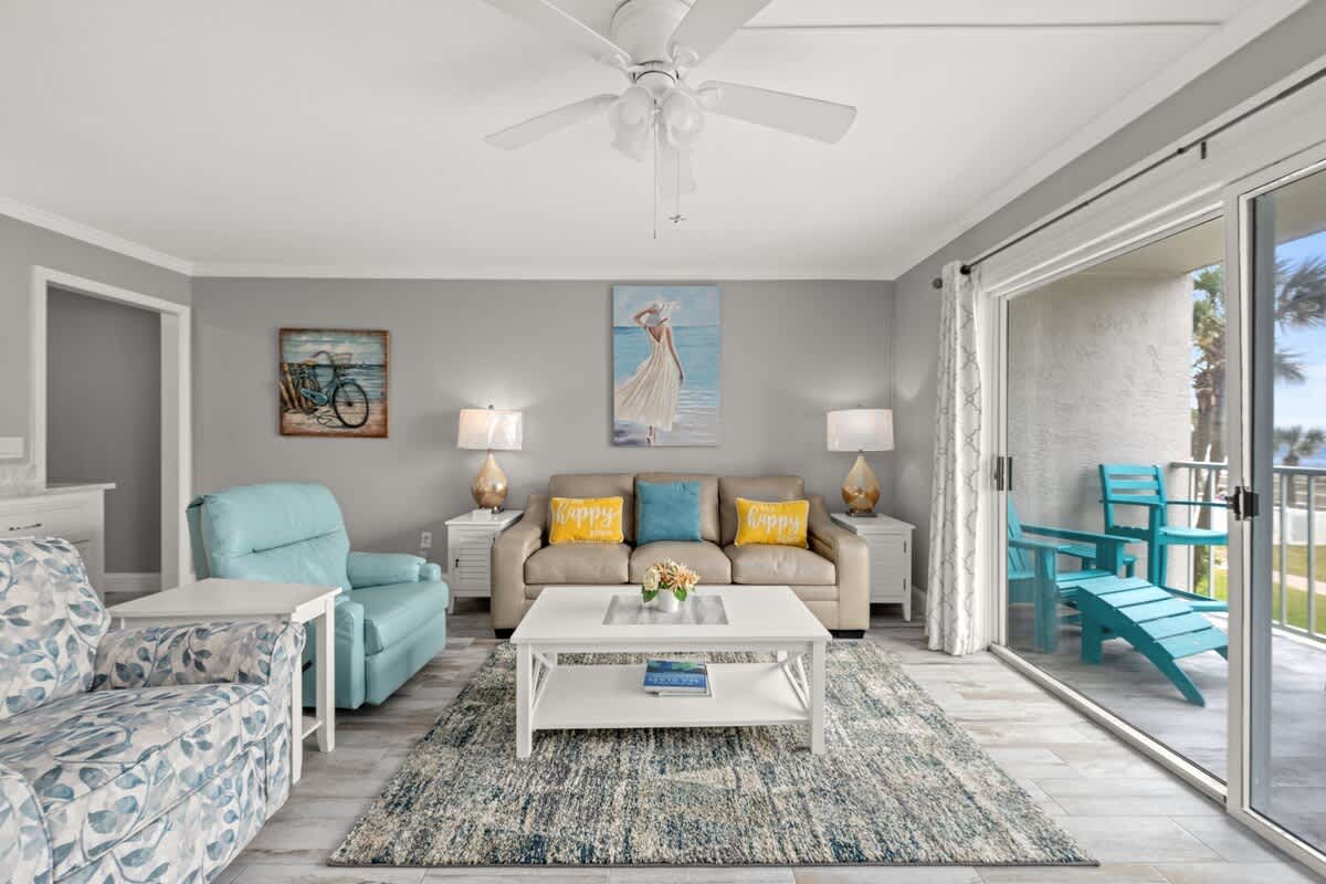 The Summit 228 – Living room with sofas, coffee table, lamps, and sliding door to balcony with blue chairs.