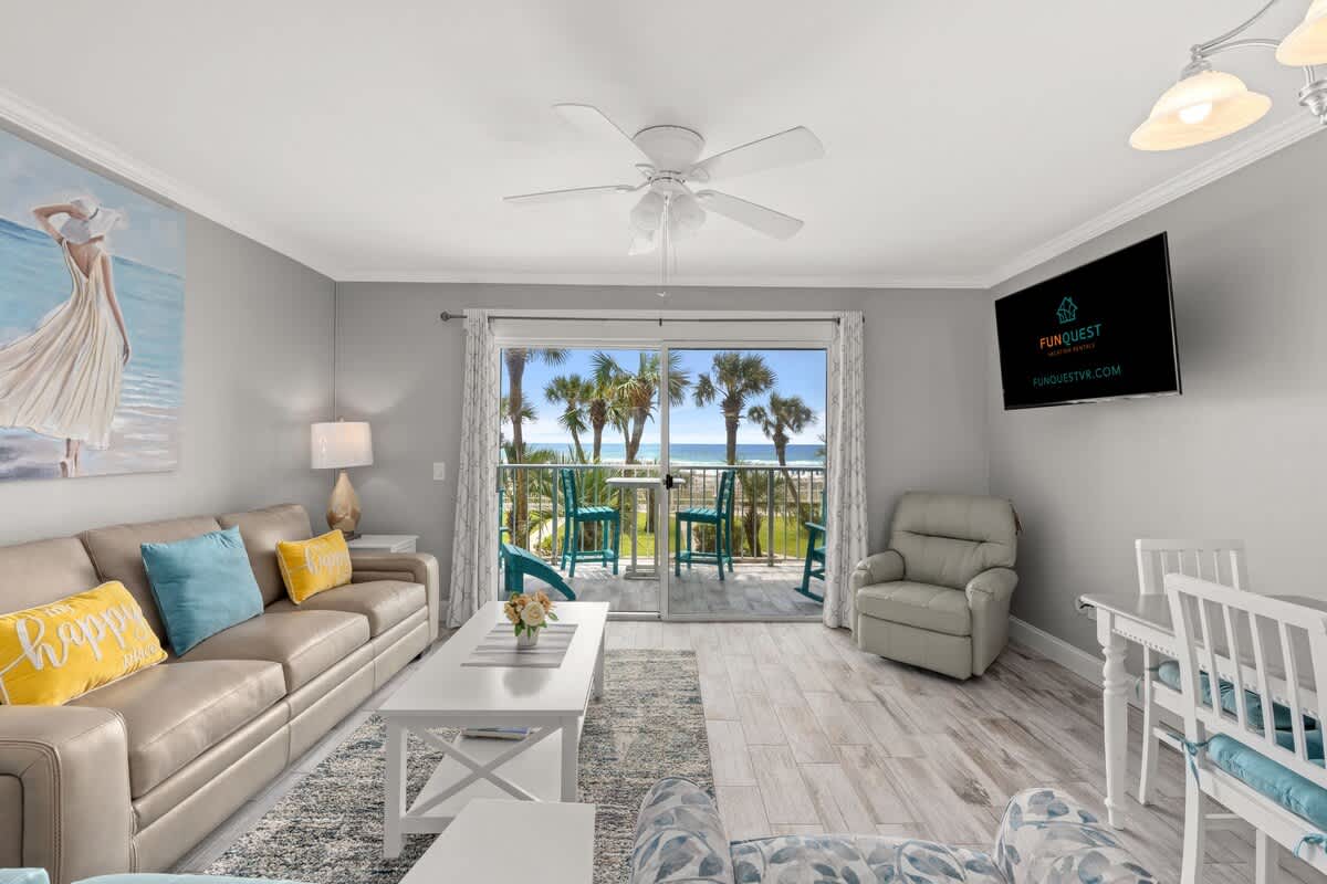 The Summit 228 – Living room with sofa, TV, and ocean view balcony featuring turquoise chairs and palm trees outside.