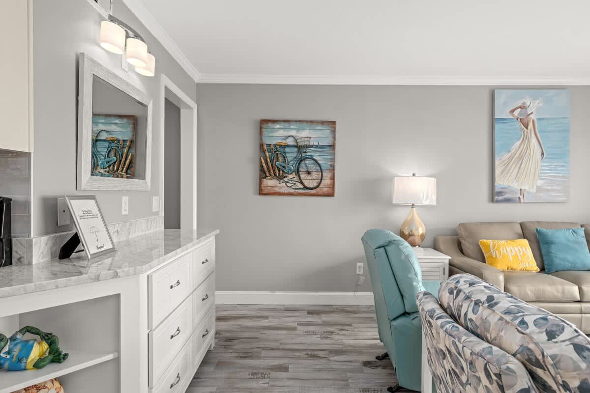The Summit 228 – Living room with modern decor, light gray walls, paintings, beige couch, and teal accent chair.