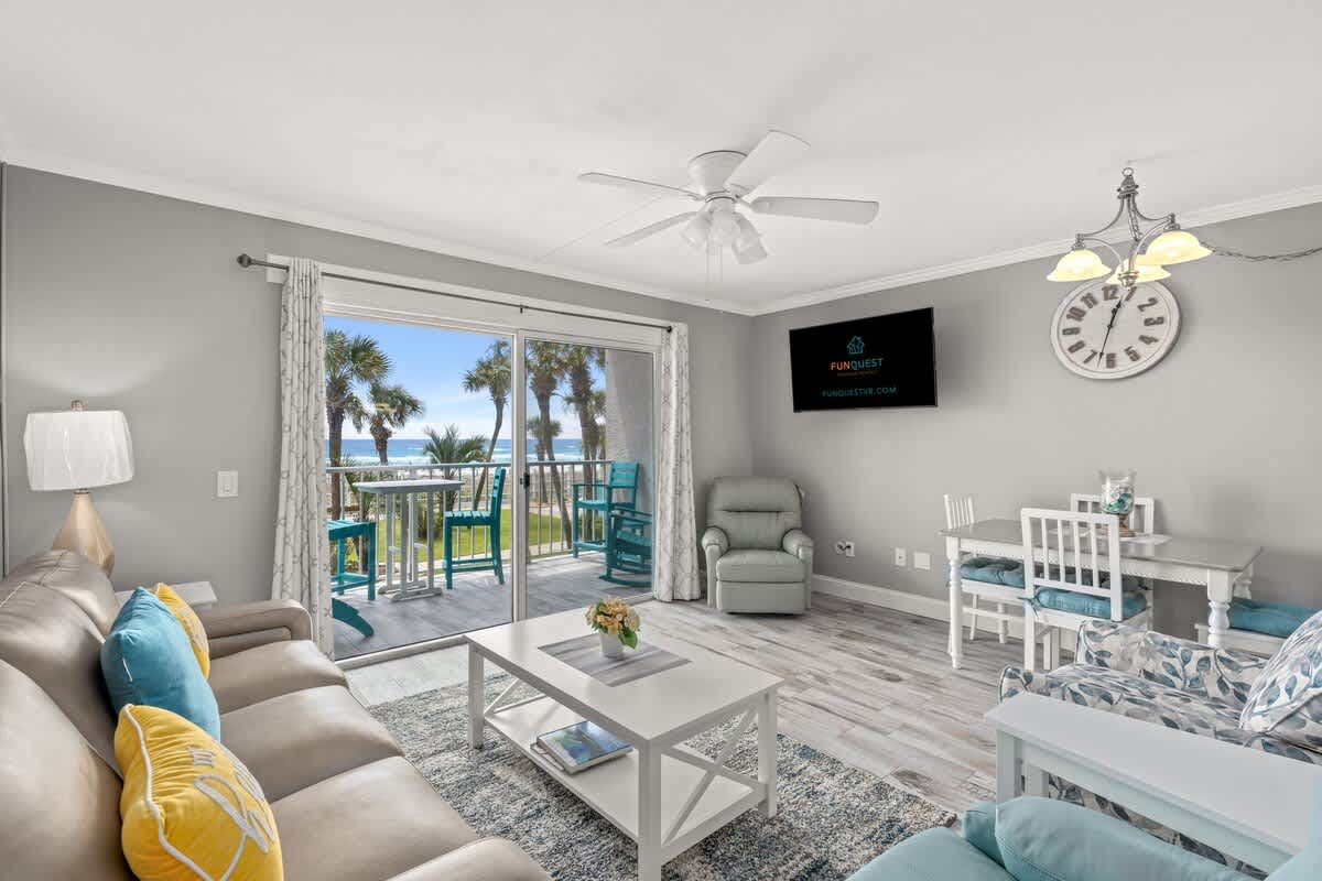 The Summit 228 – Living room with beach view, sofa, chair, dining table, and sliding glass doors to a balcony.