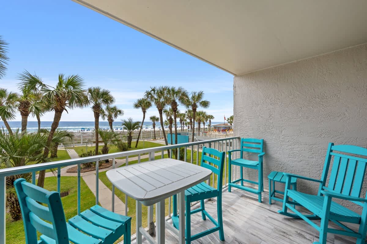 The Summit 228 – Balcony with teal furniture overlooking palm trees and the ocean.