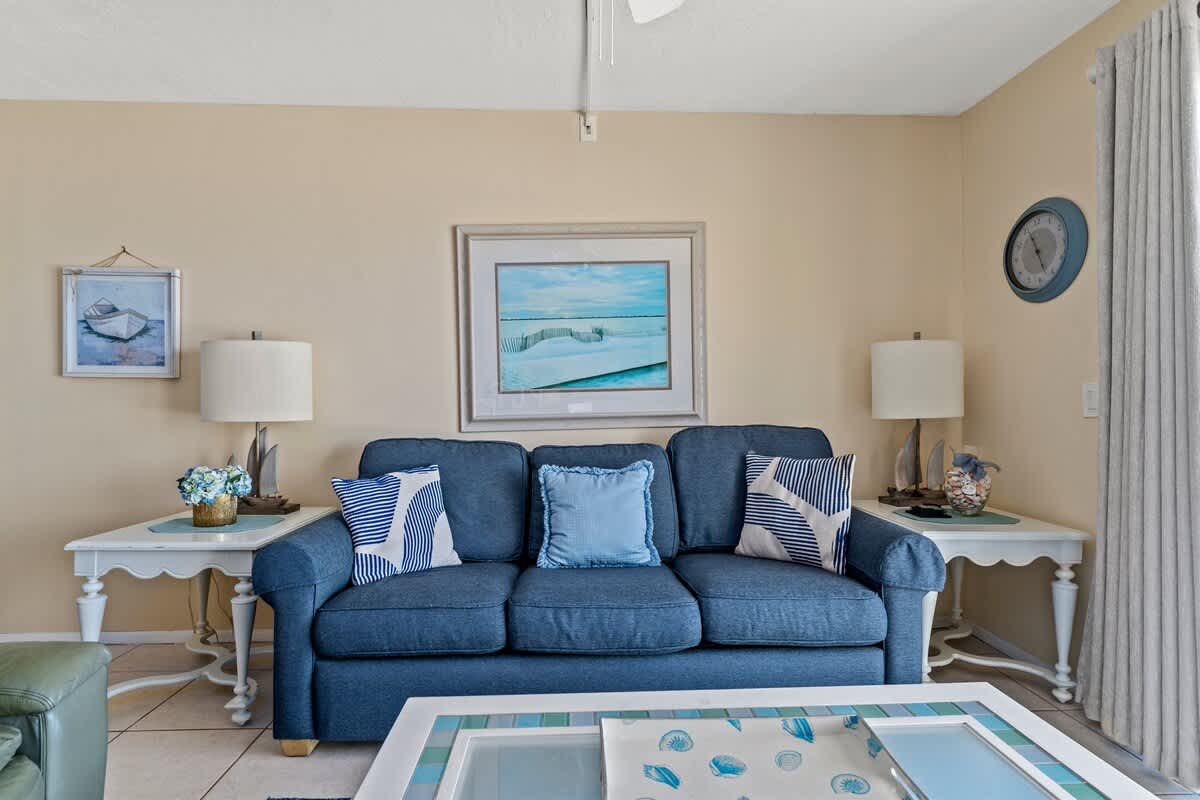The Summit 506 – Living room with blue sofa, decorative pillows, side tables, lamp, and wall art.