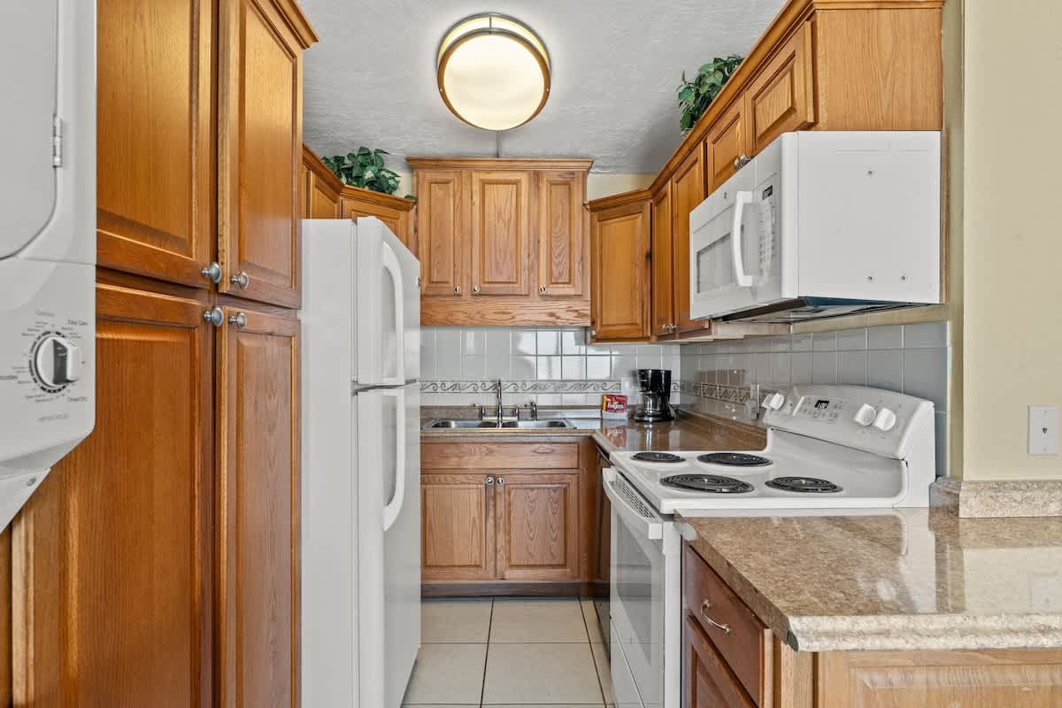 The Summit 506 – Kitchen featuring wooden cabinets, white appliances, and a granite countertop.