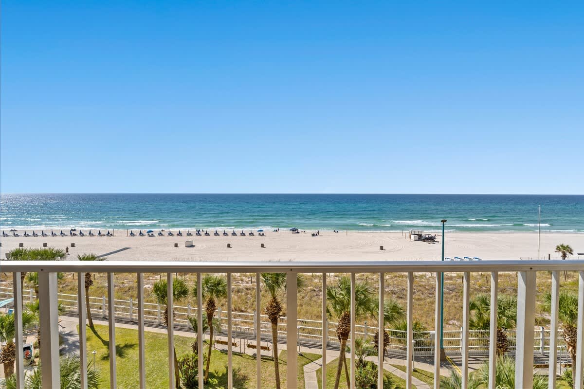 The Summit 506 – Beach view from balcony, white sand, lined with blue lounge chairs and palm trees.