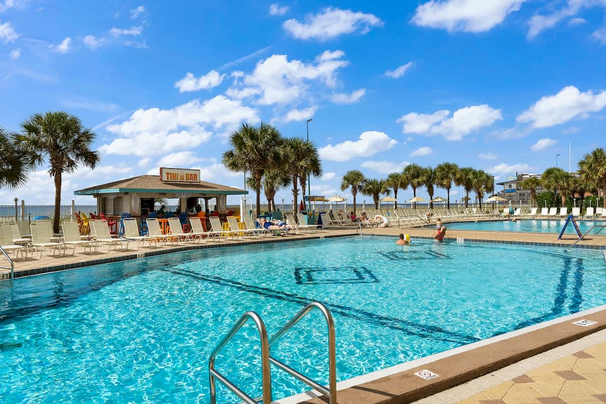 The Summit 506 – Swimming pool with lounge chairs, a tiki bar, and palm trees under a blue sky.