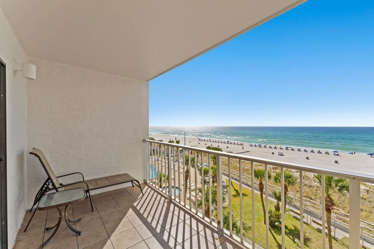 The Summit 506 – Balcony view overlooking the beach with lounge chairs and palm trees.
