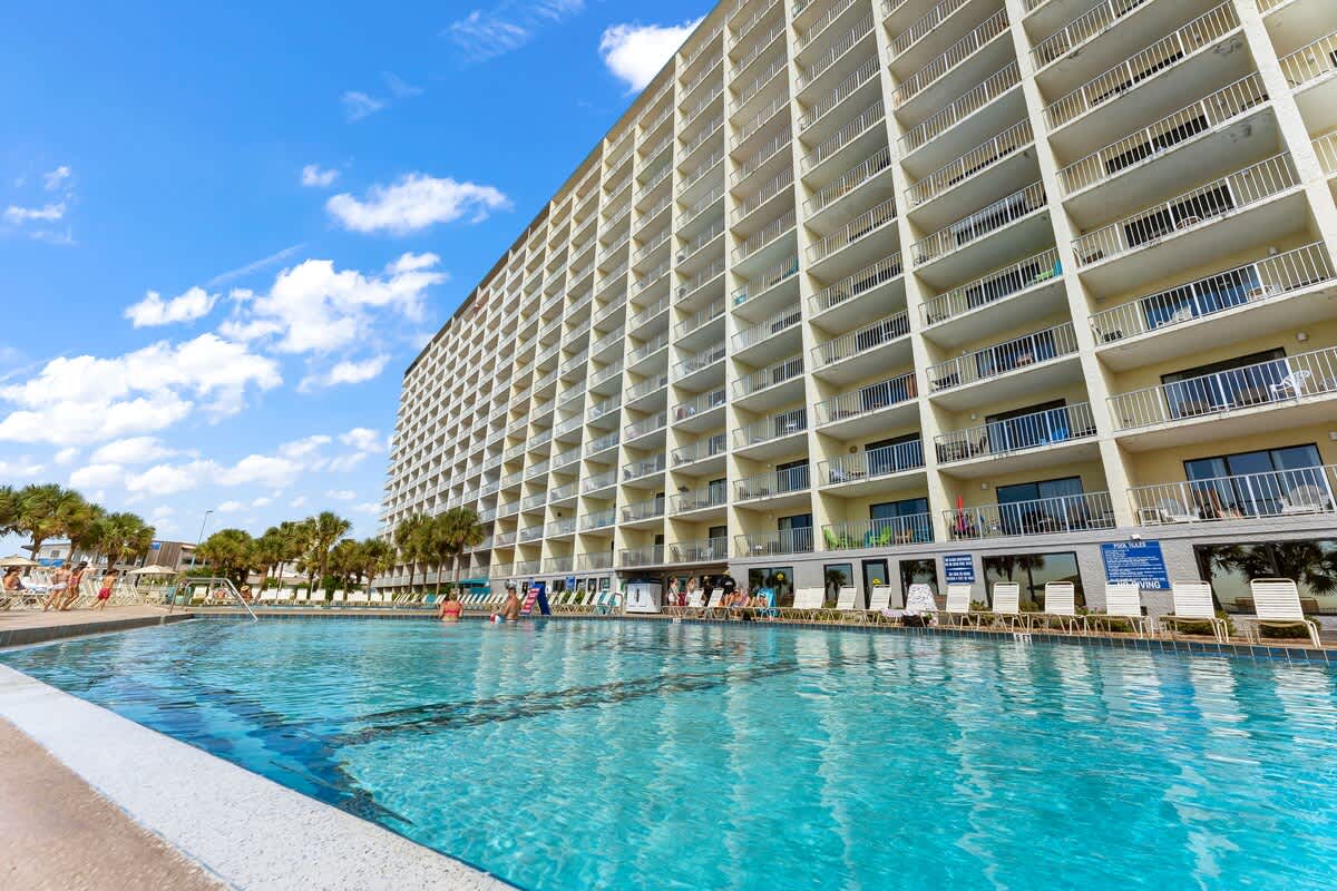 The Summit 506 – Poolside view of a multi-story vacation rental with balconies and palm trees under a blue sky.