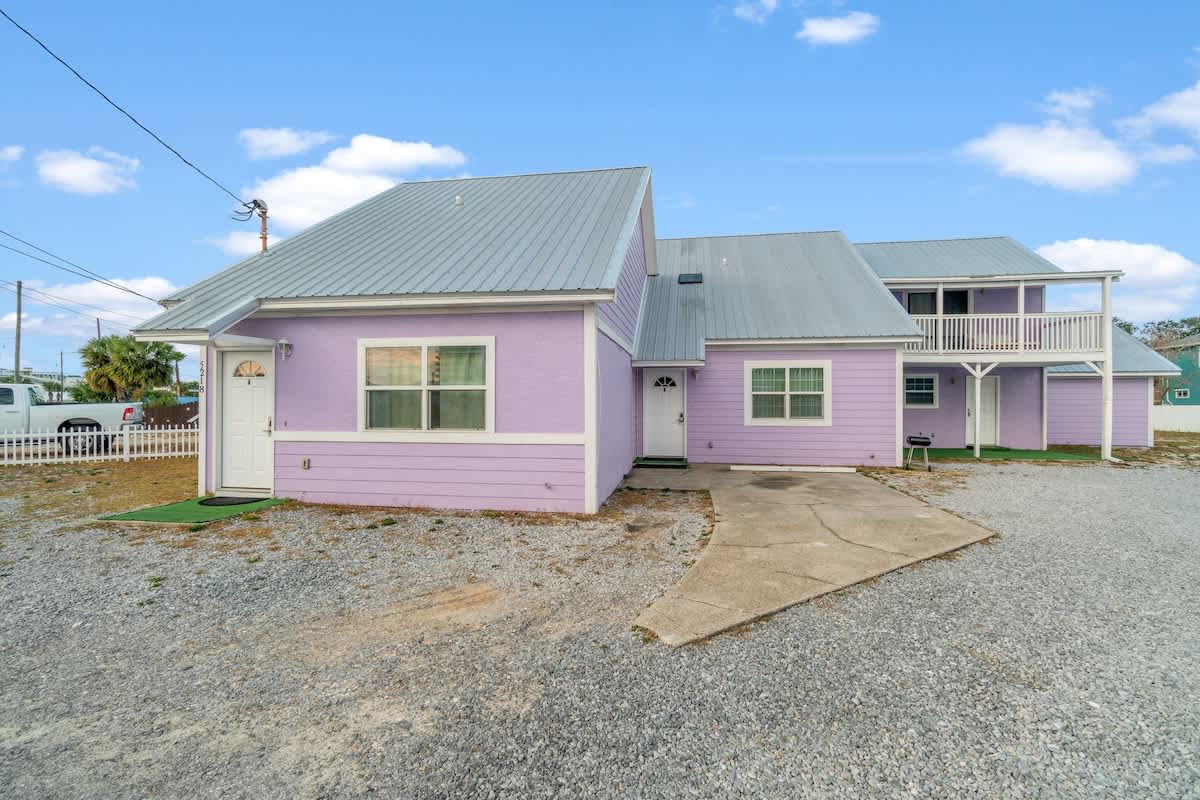 5218 Beach Dr A – Purple vacation rental with a metal roof, gravel parking, and patio area.