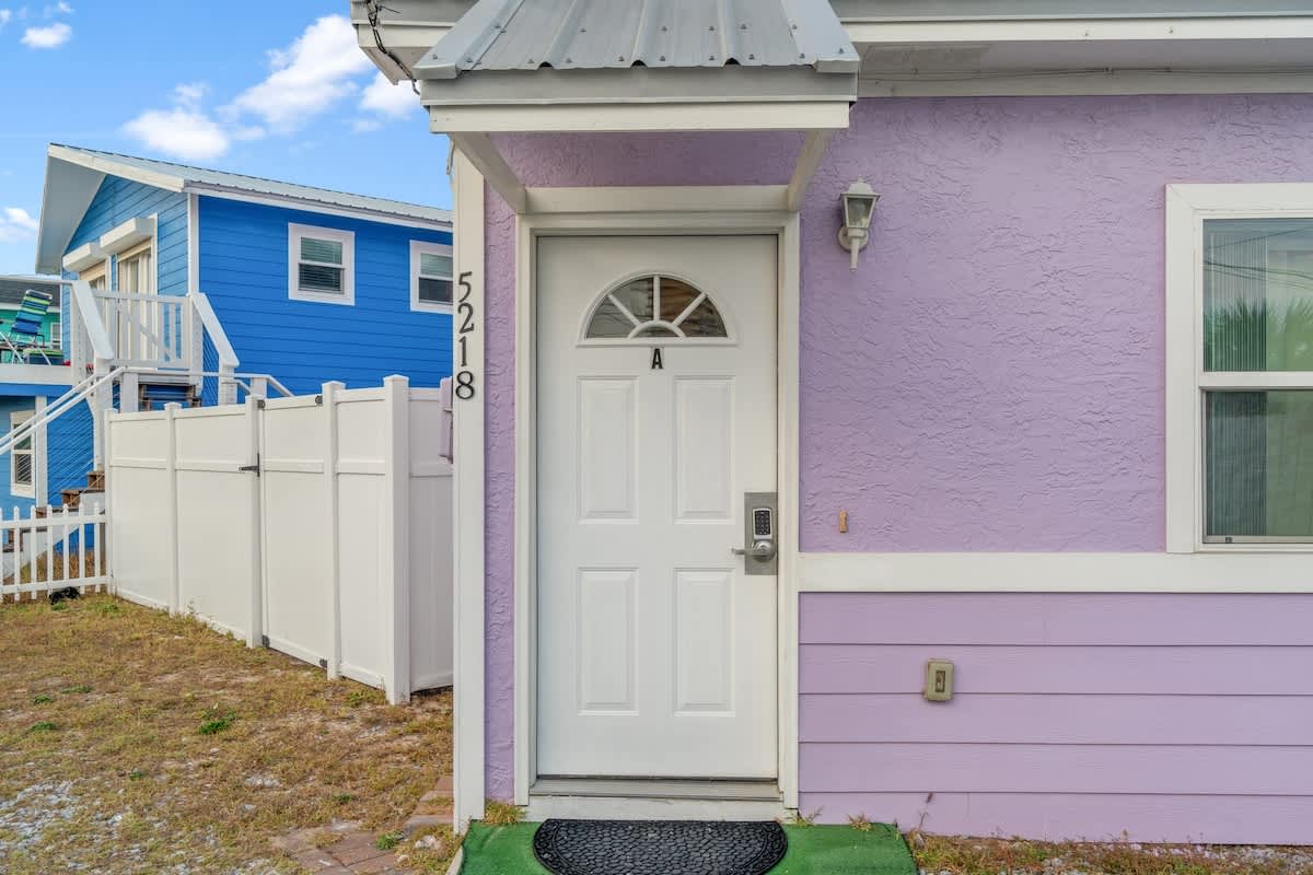 5218 Beach Dr A – Entrance to a small purple vacation rental with a door and window, surrounded by a white fence.
