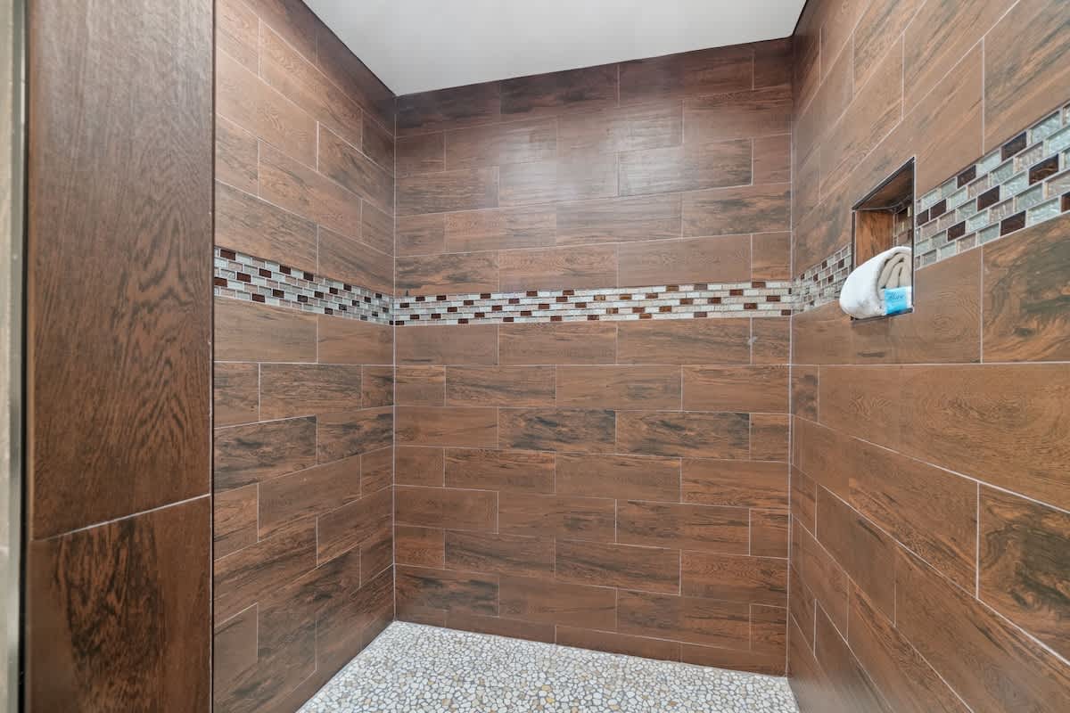 5218 Beach Dr A – Shower with wooden-style tiles, mosaic accent strip, and pebble-style floor.