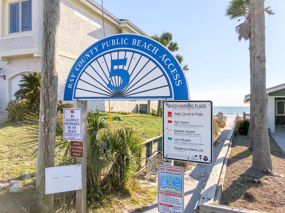 5218 Beach Dr A – Sign for public beach access with warning flags and pathway leading to the beach.