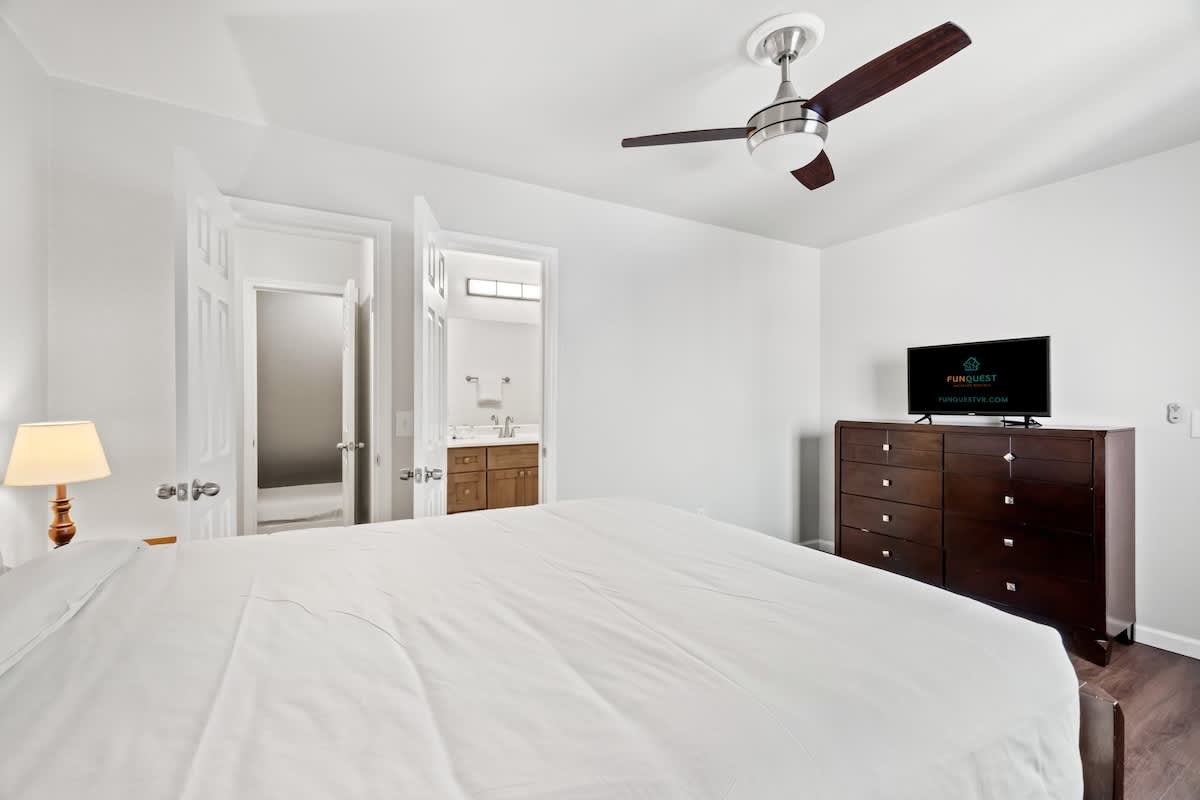 5218 Beach Dr A – Bedroom with a large bed, dresser, TV, ceiling fan, and bathroom doorway.