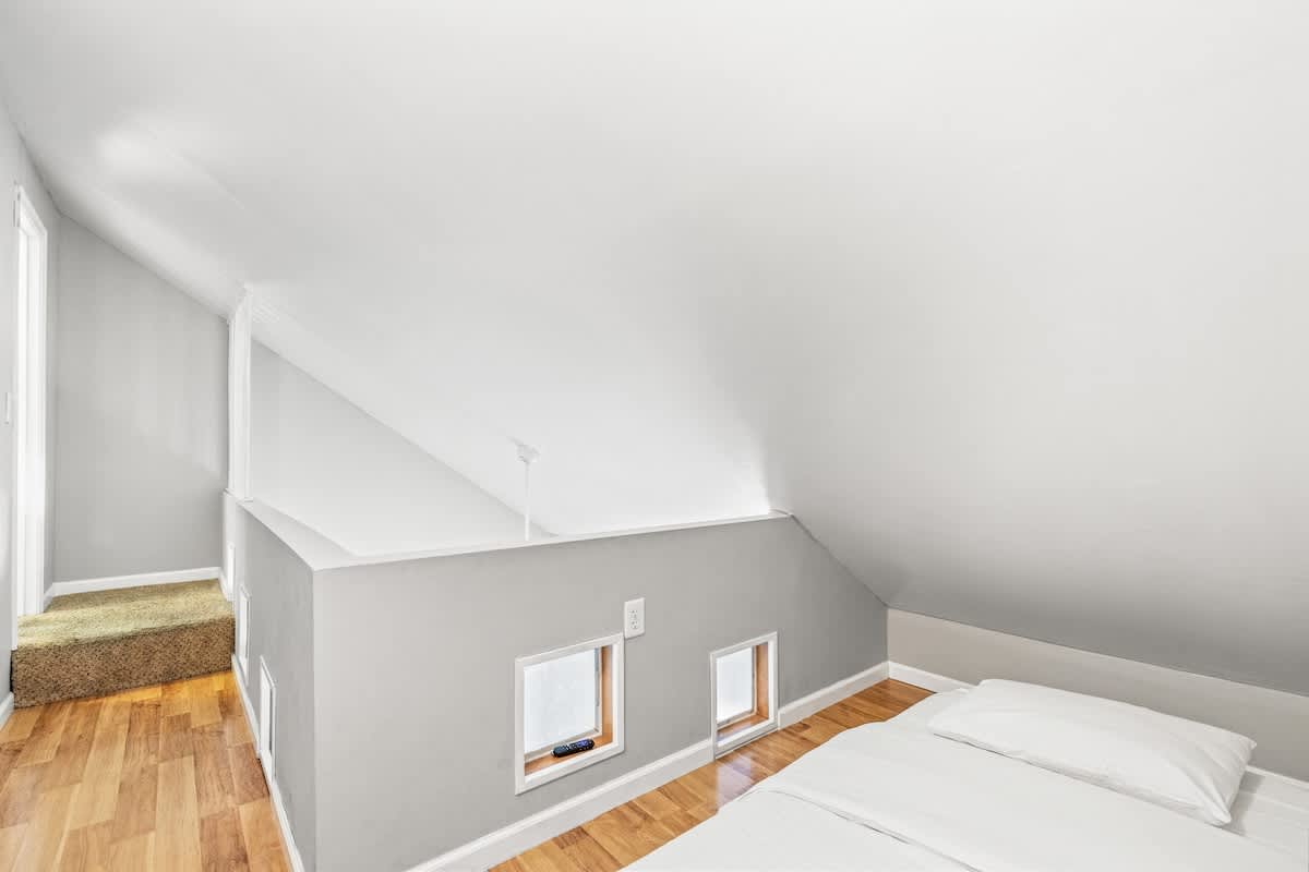 5218 Beach Dr C – Loft bedroom with low sloped ceiling, wooden floor, two small windows, and a bed with white linens.