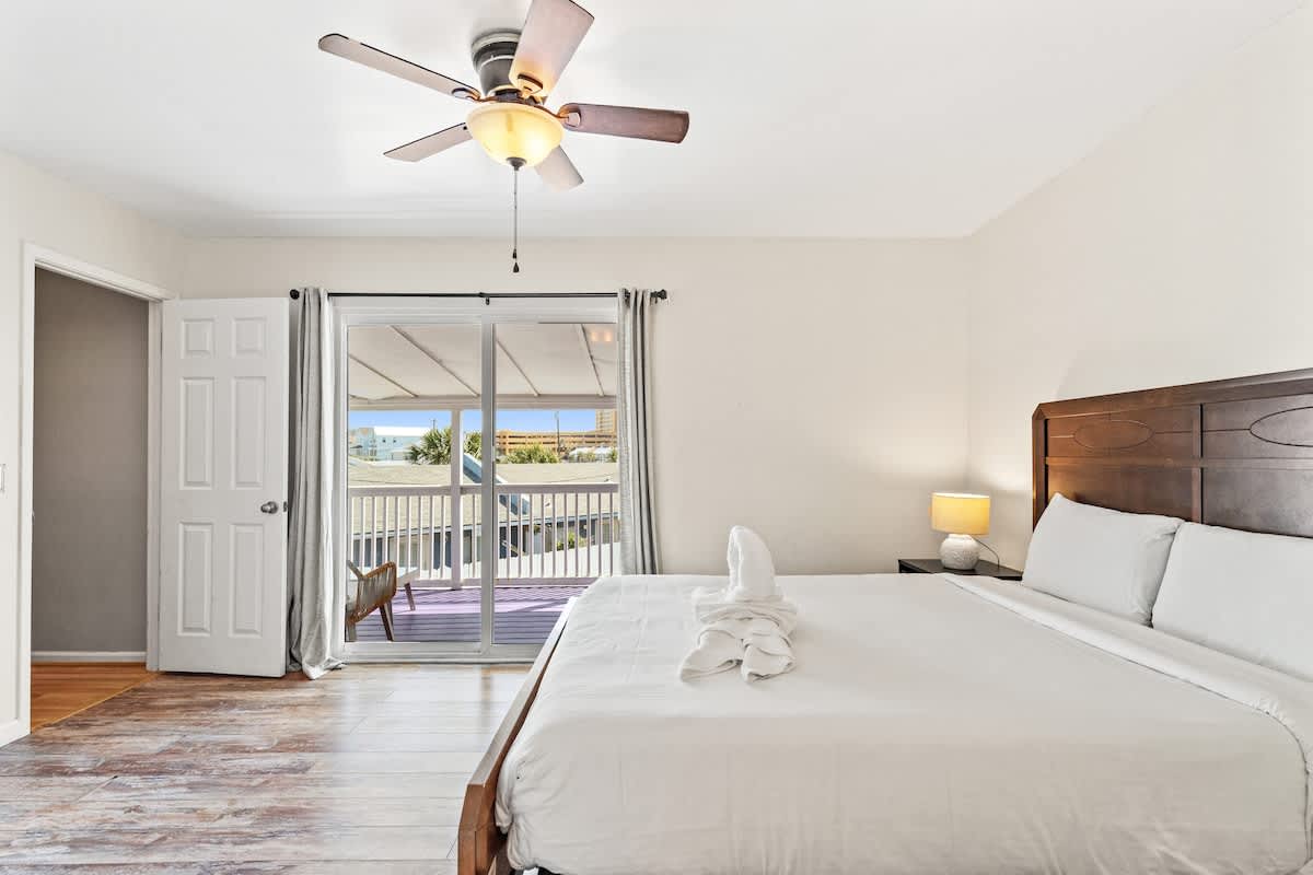 5218 Beach Dr C – Bright bedroom with a queen bed, ceiling fan, and sliding glass doors to a balcony with a beach view.