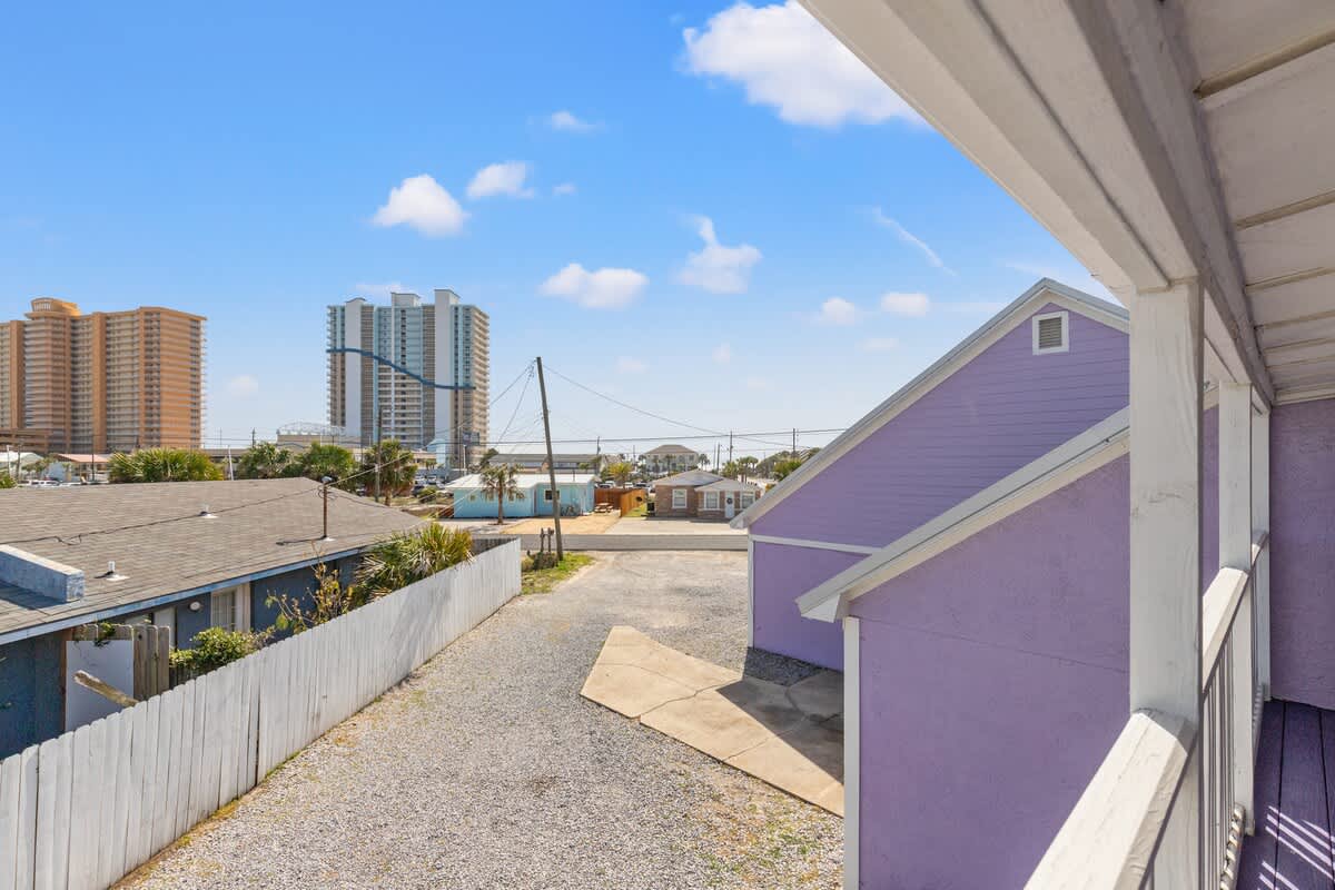 5218 Beach Dr C – View from balcony showing nearby buildings, gravel driveway, and a purple rental house.