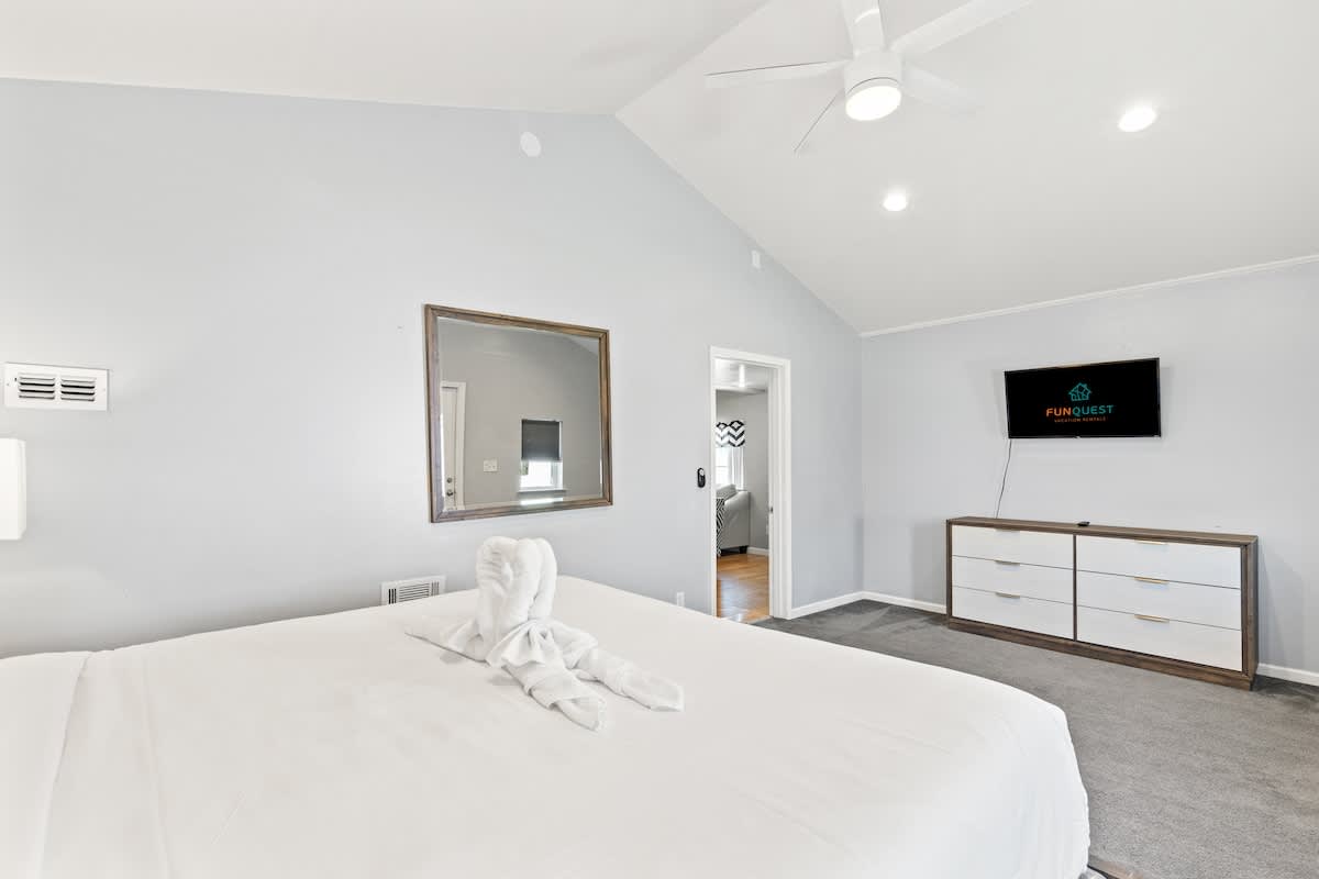 5218 Beach Dr C – Bright bedroom with a large bed, mirror, TV, and doorway to another room.