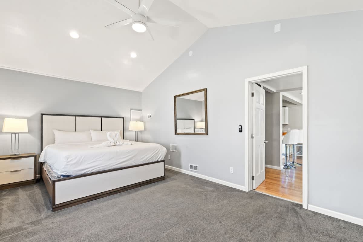 5218 Beach Dr C – Spacious bedroom with a king bed, two lamps, and an adjoining door to another room.