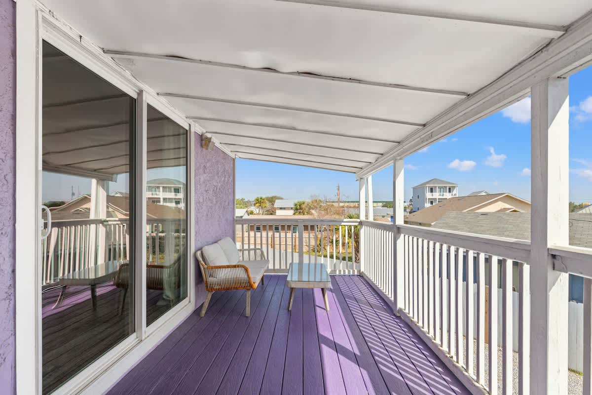 5218 Beach Dr C – Covered porch with purple flooring, featuring a seating area and views of nearby houses and blue sky.