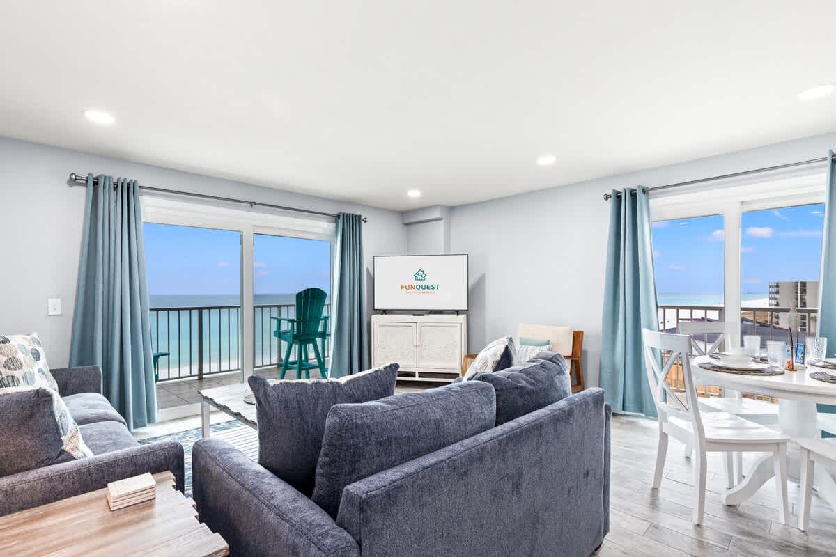 The Summit 701 – Living room with ocean view, blue sofas, dining table, and balcony access.