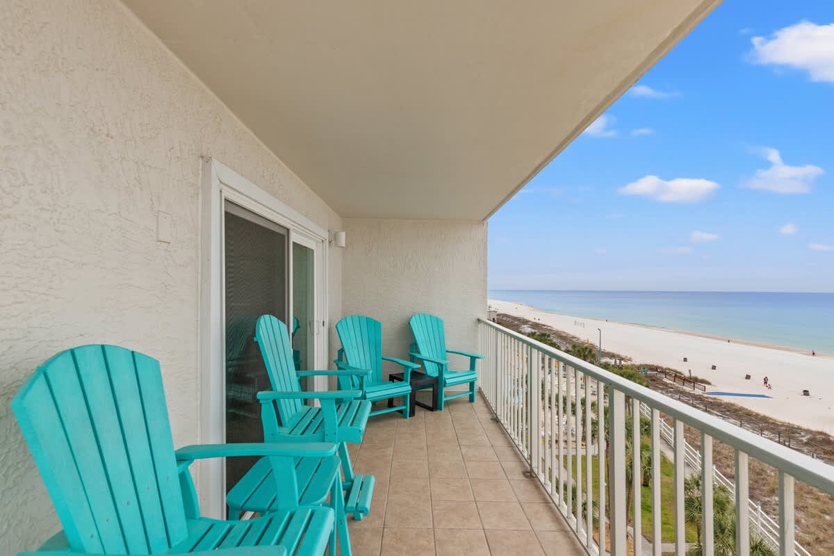 The Summit 701 – Balcony with four teal chairs overlooking a sandy beach and calm ocean water.