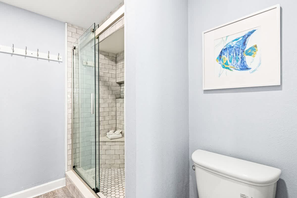 The Summit 701 – Bathroom featuring a glass shower, white toilet, and framed fish artwork on light blue walls.