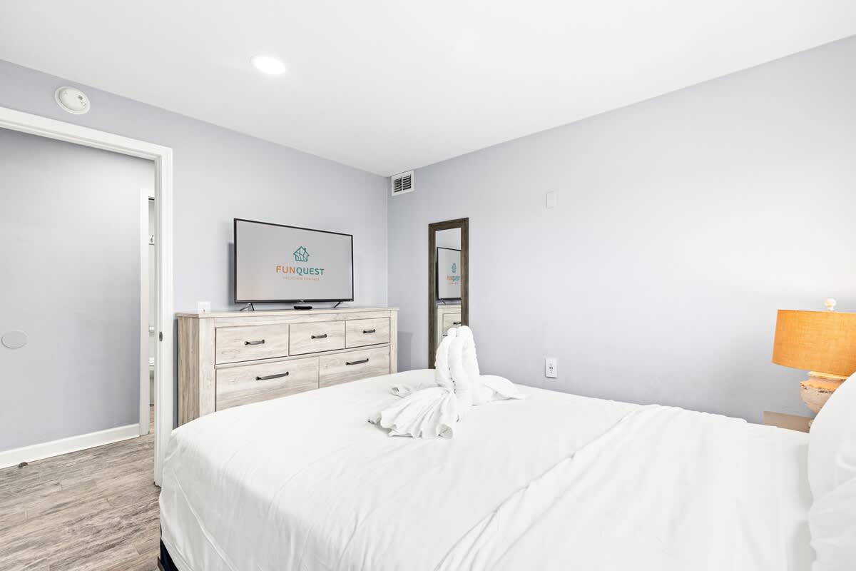 The Summit 701 – Cozy bedroom with a TV, dresser, lamp, and decorative towel on the bed.
