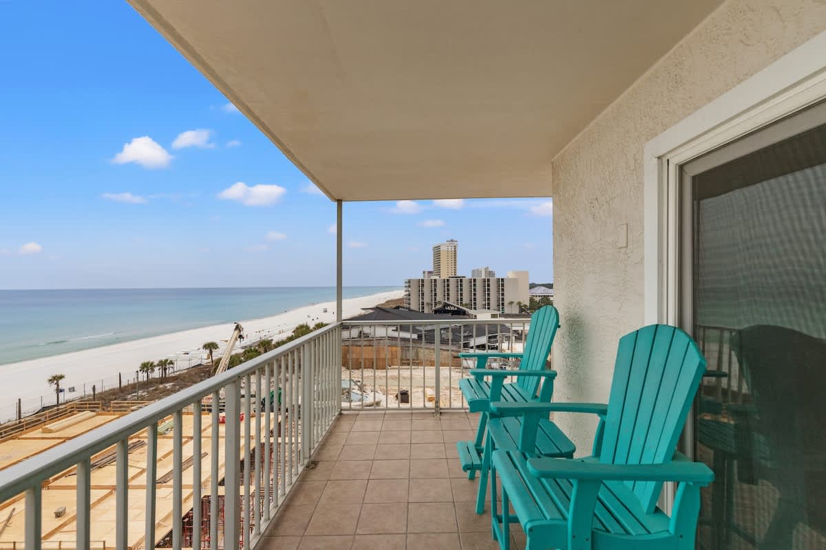 The Summit 701 – Balcony view of the beach with turquoise chairs and nearby buildings.