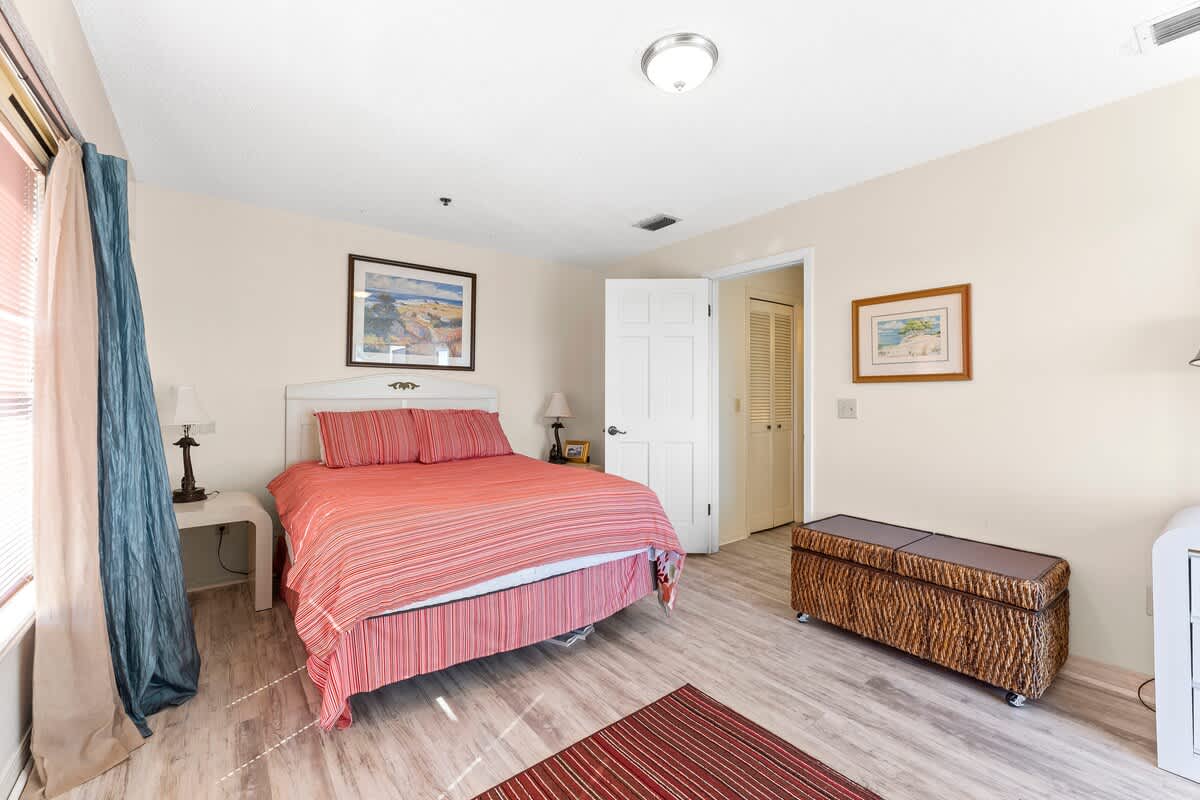 St Thomas SQ 1302B – Bedroom with a striped bedspread, nightstand, artwork, and a bench in a light-colored room.