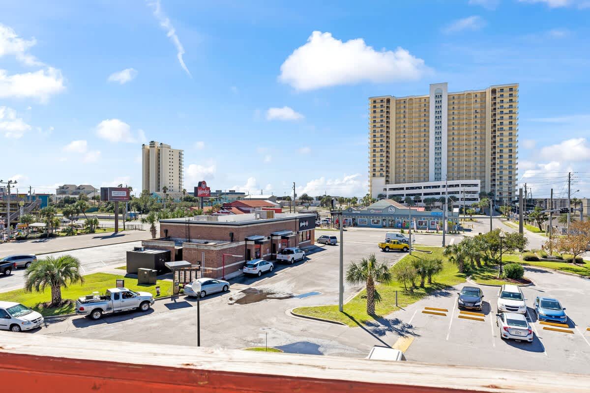 St Thomas SQ 1302B – View from a balcony overlooking parking lot, buildings, and palm trees under sunny skies.