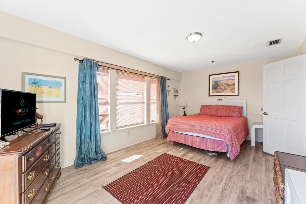 St Thomas SQ 1302B – Bright bedroom with a queen bed, colorful bedding, dresser, TV, and large windows with natural light.