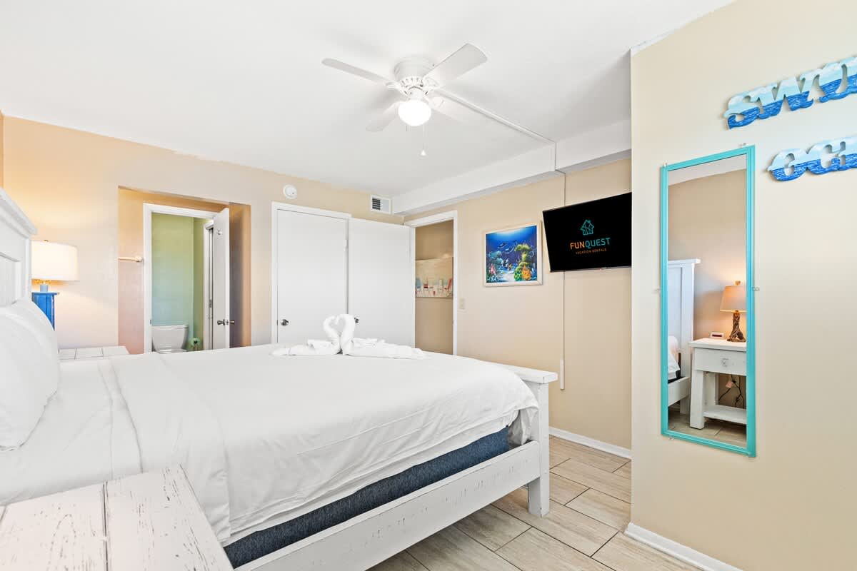 The Summit 1011 – Bright bedroom with a queen bed, ceiling fan, TV, and ensuite bathroom door visible.