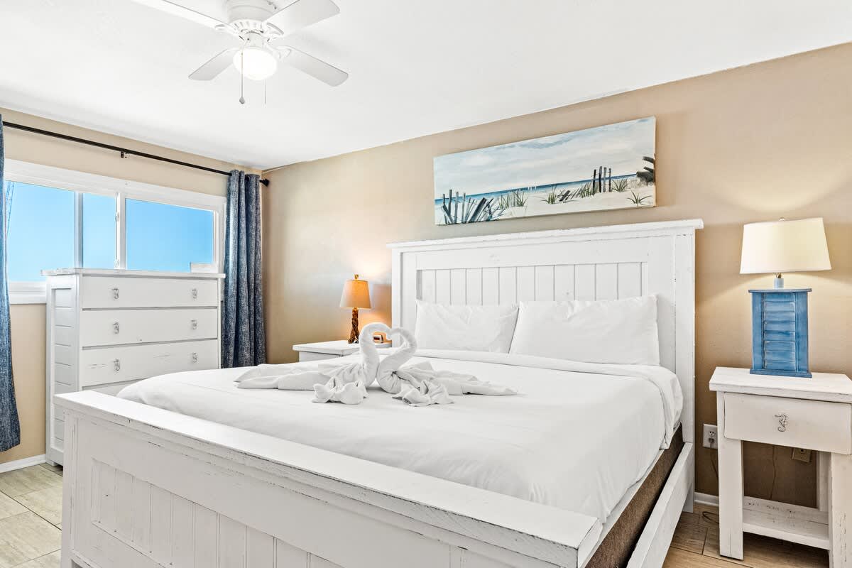 The Summit 1011 – Bright bedroom with a queen bed, dresser, nightstand, and view of blue sky through window.