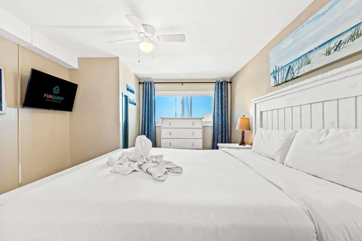 The Summit 1011 – Bright bedroom with a king bed, TV, dresser, windows, and ocean view.