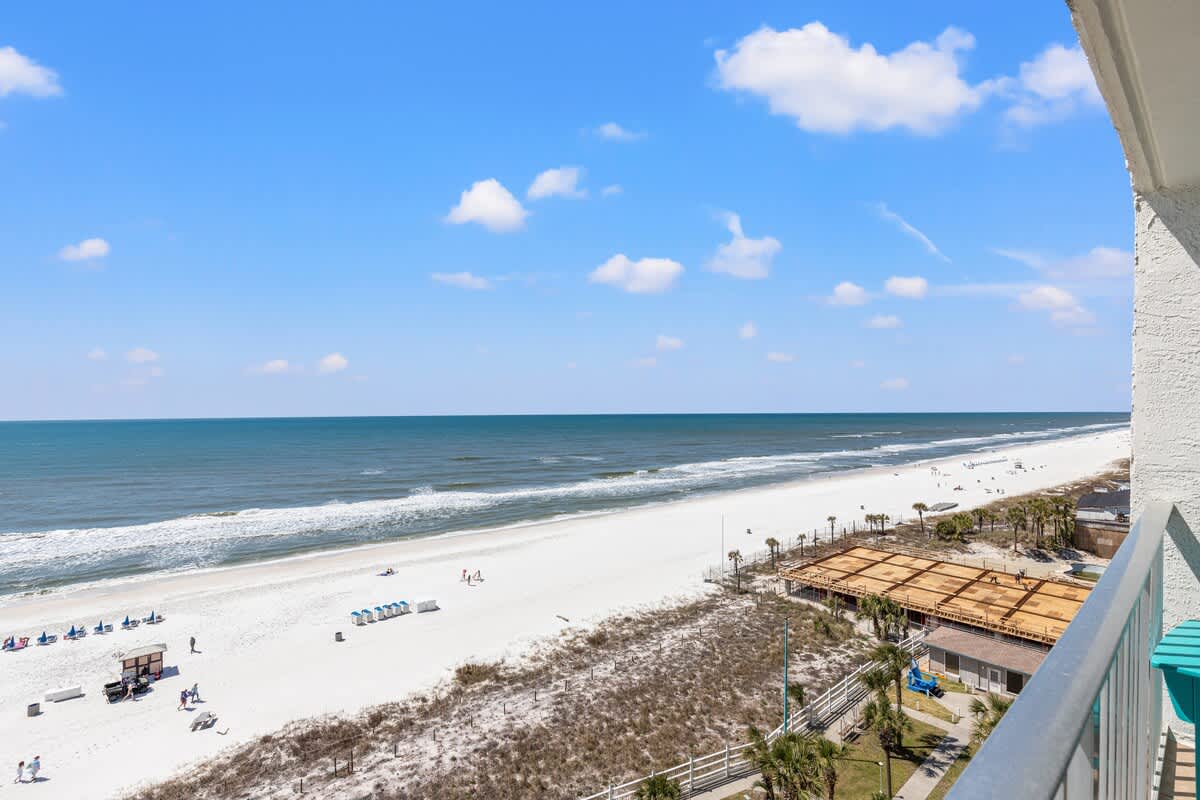 The Summit 1011 – Ocean view from balcony with white sandy beach and blue water, featuring beachgoers and umbrellas.