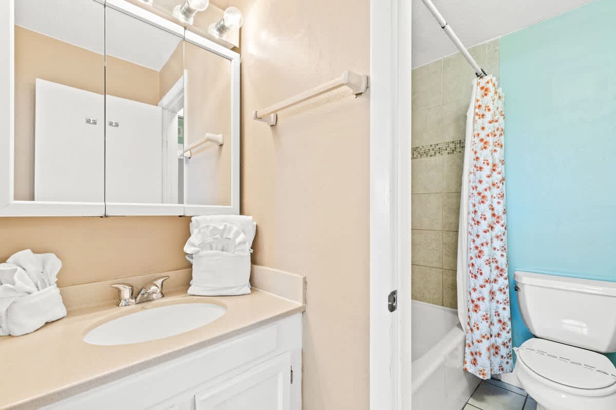 The Summit 1011 – Bathroom with a sink, mirror, toilet, and shower curtain featuring floral design.