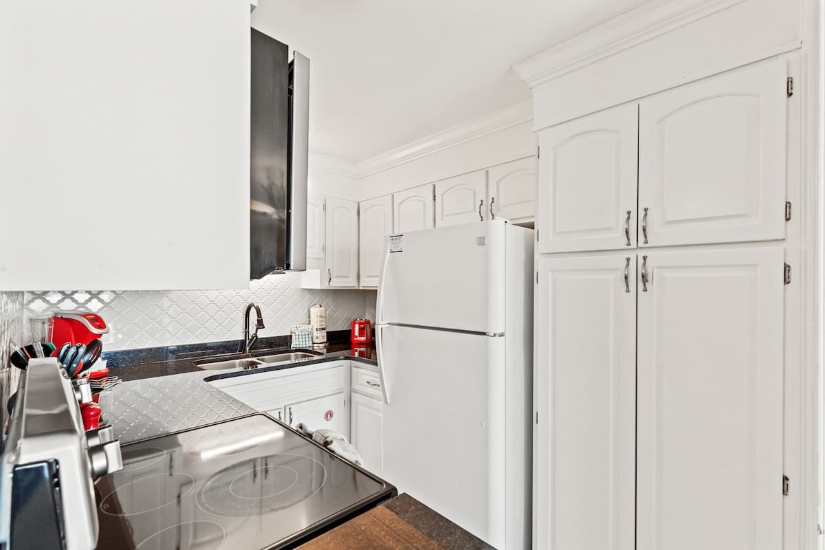 The Summit 1121 – Compact kitchen with white cabinets, black countertops, stove, refrigerator, and red appliances.