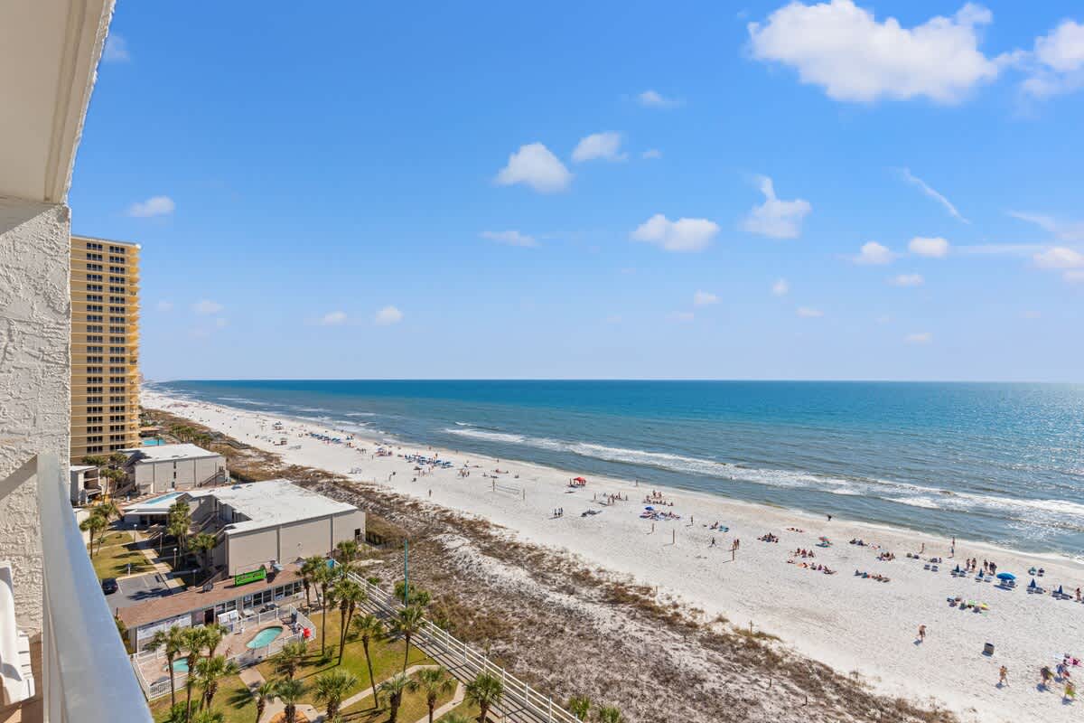 The Summit 1122  – Ocean view from a balcony overlooking sandy beach and coastline with sunbathers and nearby palm trees.