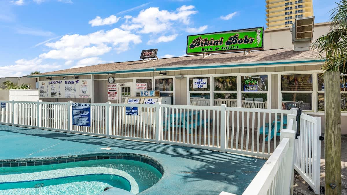 The Summit 1122  – Outdoor bar and grill with pool area, featuring a sign for Bikini Bob's, surrounded by white fencing and palm trees.