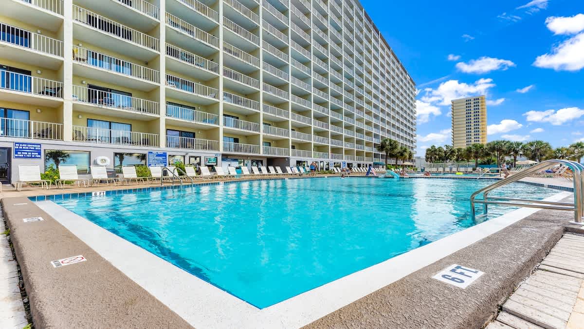 The Summit 1122  – Pool area with lounge chairs and a multi-story building in the background under a blue sky.