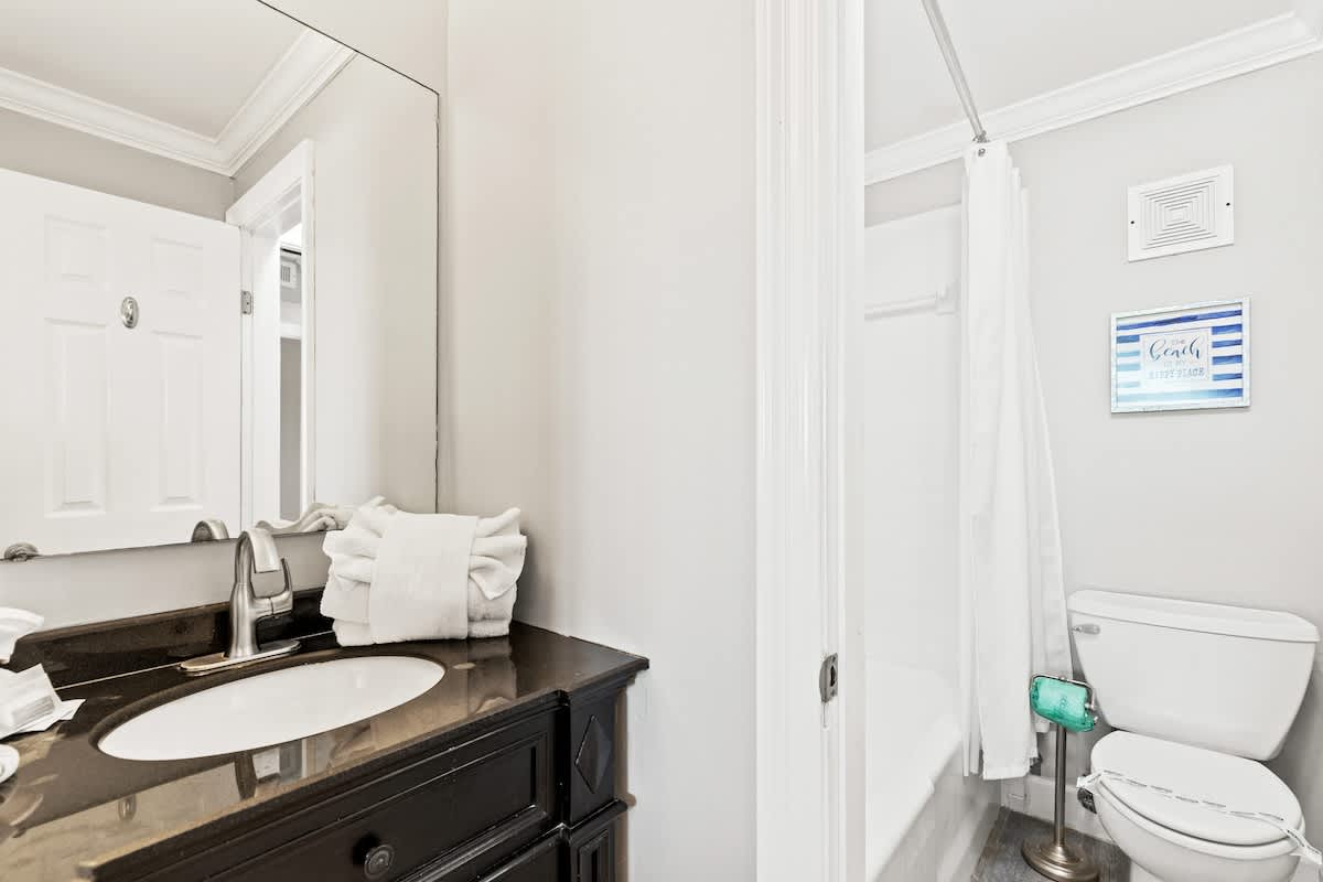 The Summit 1121 – Bathroom with a dark countertop, sink, mirror, and shower tub combination. White towels neatly stacked.