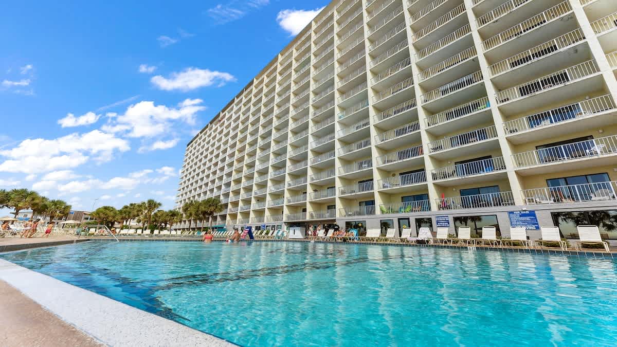 The Summit 1122  – Poolside view of a multi-story vacation rental with balconies and palm trees.