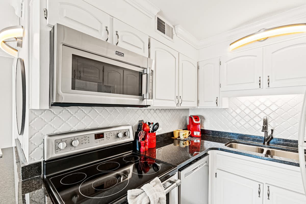 The Summit 1121 – Kitchen with white cabinets, black granite countertops, stainless steel appliances, and a red coffee maker.