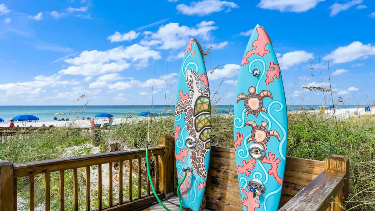 The Summit 1122  – Two colorful surfboards beside a beach path, with a view of umbrellas and ocean in the background.