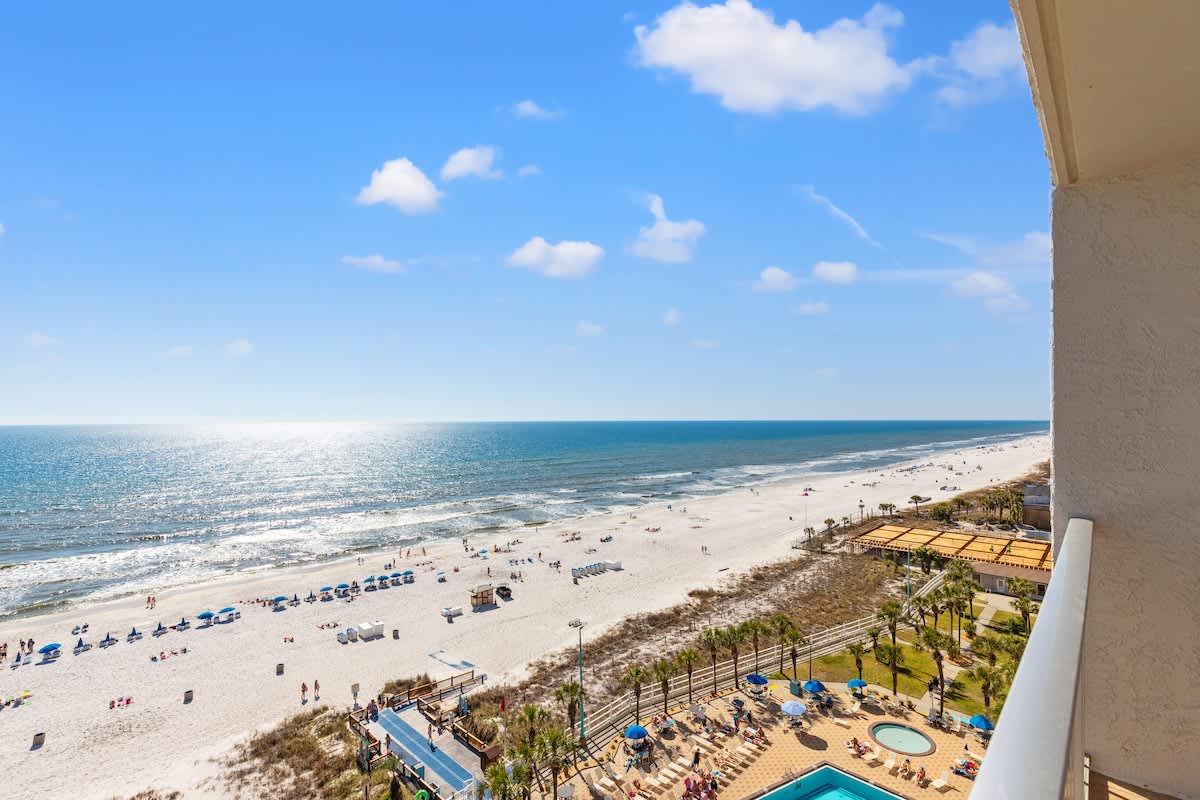 The Summit 1122  – Ocean view from a balcony, beach, pool area, and sun loungers visible below.