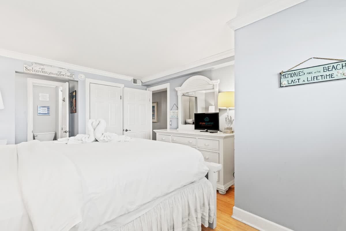 The Summit 1121 – Bright bedroom with a white bed, dresser, lamp, and decorative signs on the walls.