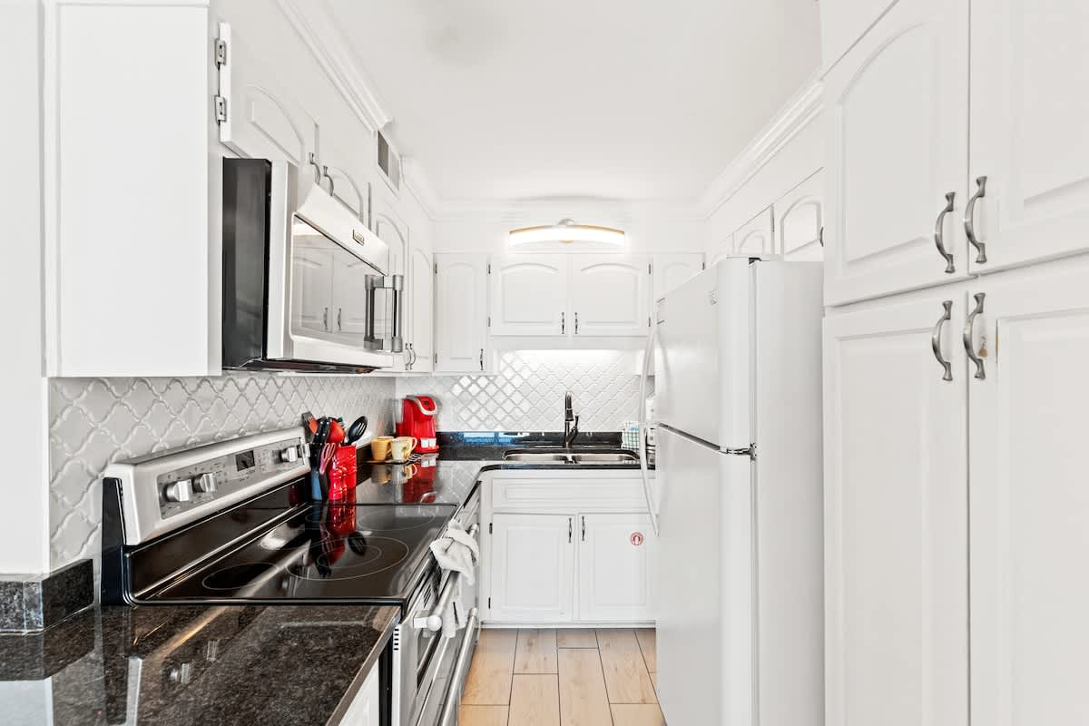 The Summit 1121 – Modern kitchen with white cabinets, black countertop, stainless steel appliances, and tile backsplash.