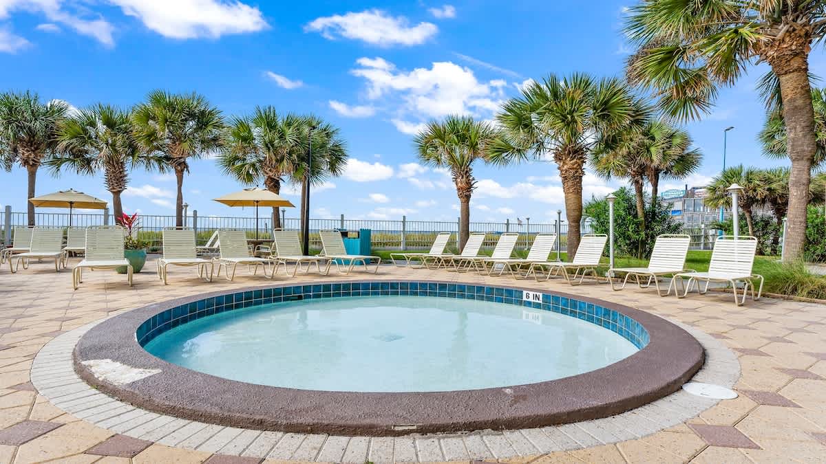 The Summit 1122  – Hot tub surrounded by palm trees, lounge chairs, and umbrellas under a blue sky.