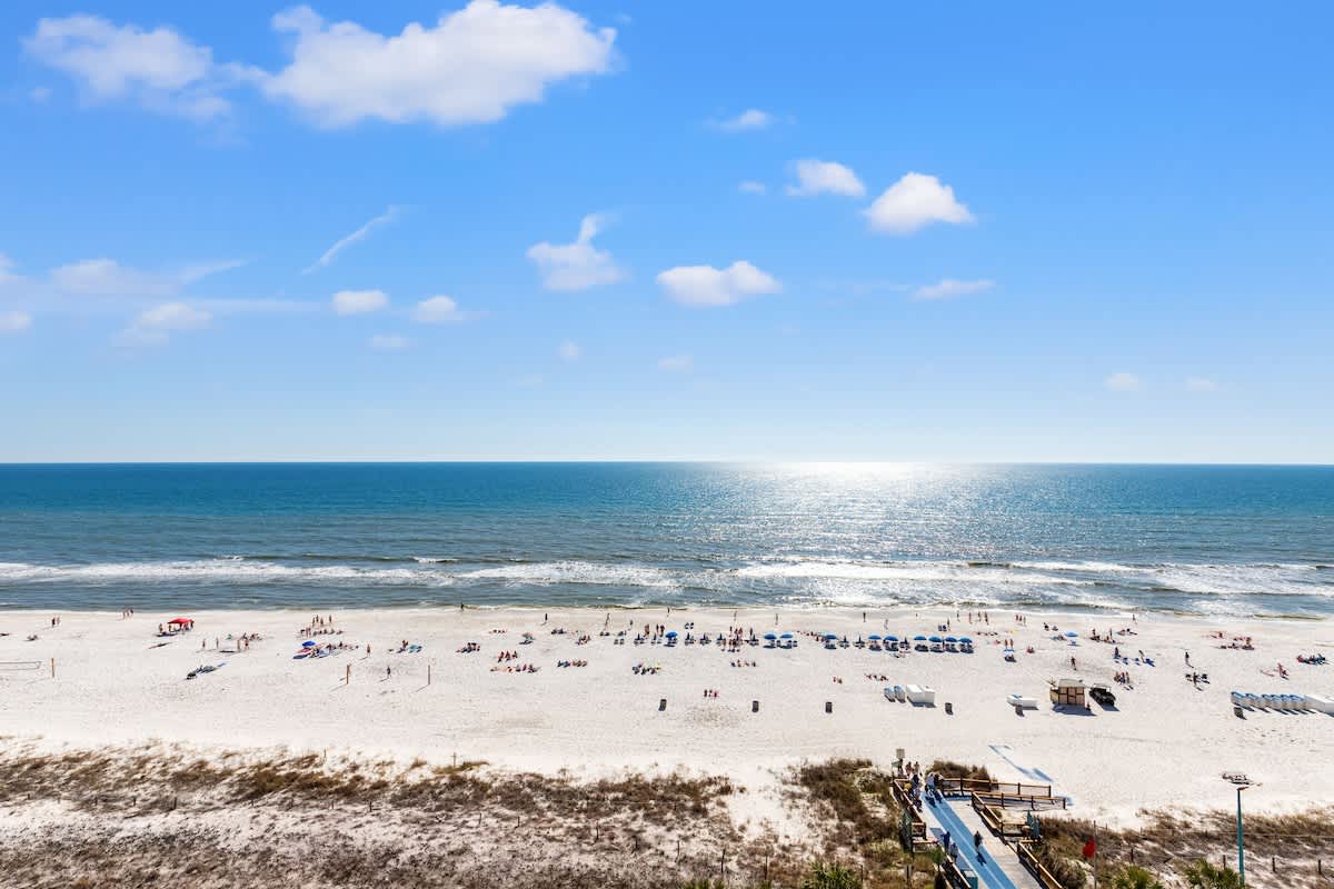 The Summit 1122  – View of beach with sun chairs, waves, and a clear blue sky from a high vantage point.