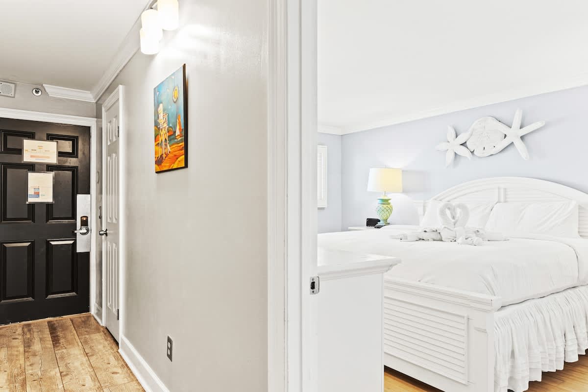 The Summit 1121 – Entryway leading to a bright bedroom with a white bed and decorative headboard.